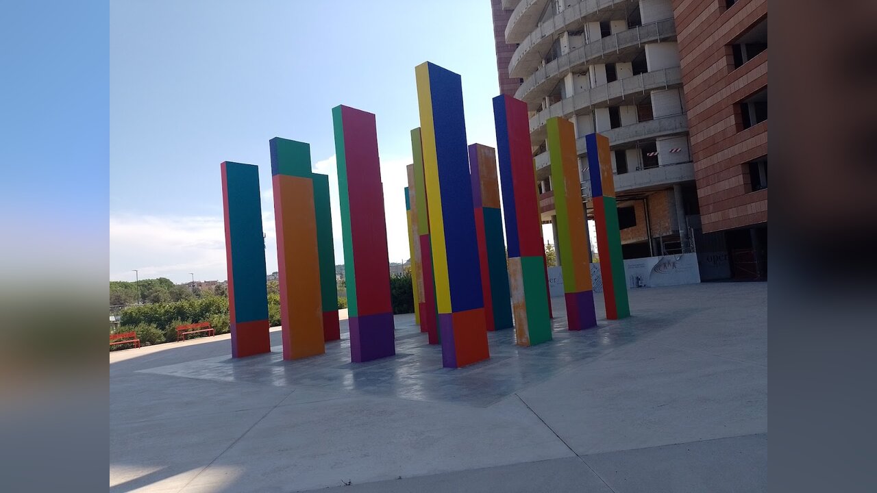 “Il giardino incantato” di Franco Summa: alti pilastri di cemento dipinti a colori vivaci in una piazza lastricata, accanto a un palazzo a più piani