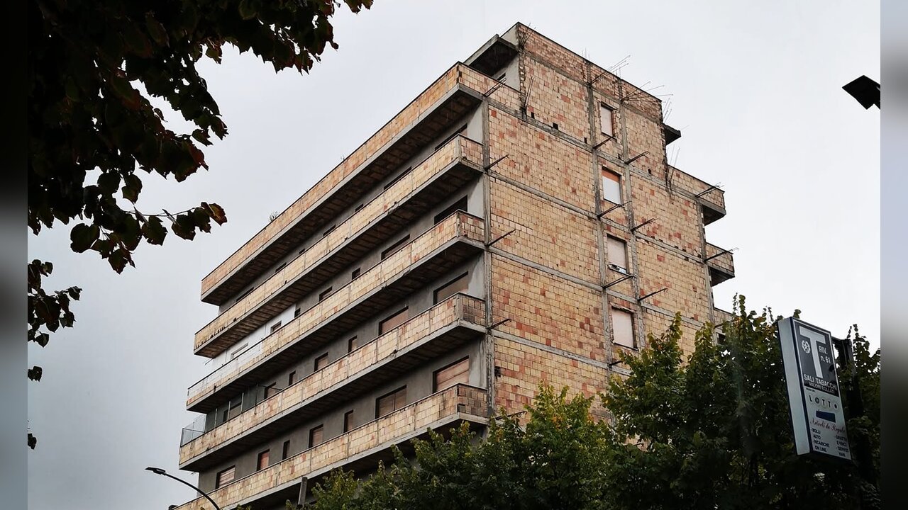 Un palazzo di diversi piani dall’aspetto trascurato, con la facciata scolorita, sotto un cielo nuvoloso