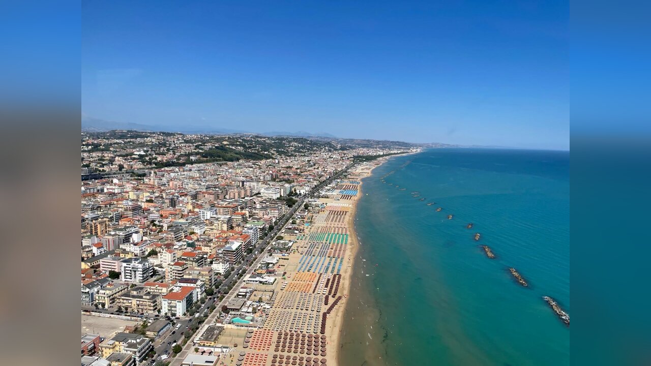 Vista aerea di Pescara: la città si estende fino alla spiaggia, coperta da file fitte di ombrelloni degli stabilimenti balneari