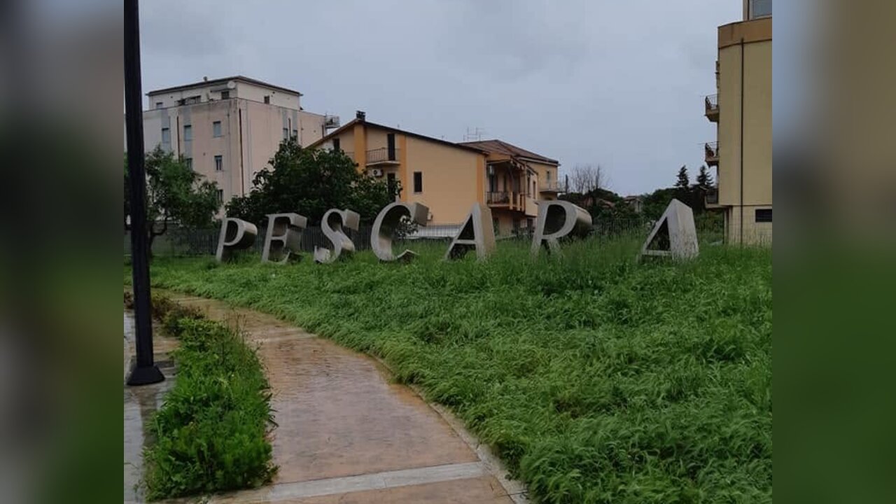 Grandi lettere che formano la scritta “PESCARA” accanto a un vialetto in un’area verde, sotto un cielo grigio
